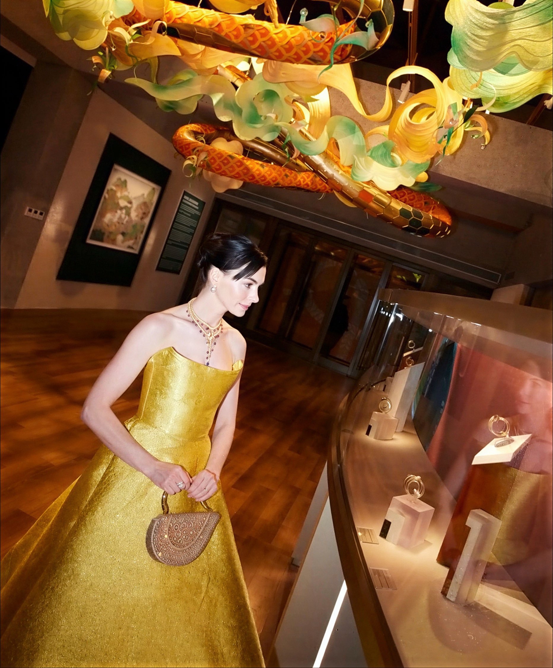 Human as a Catalyst — guest in a gold gown browsing the interactive stations beneath the serpent sculpture